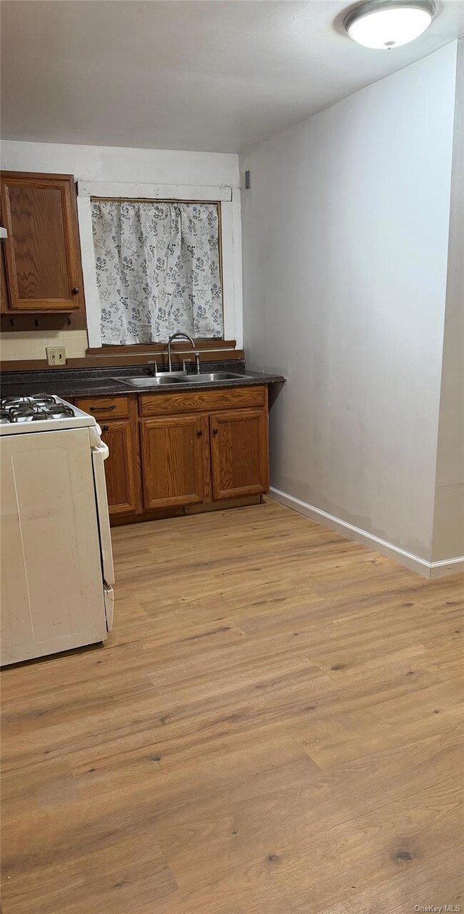 Kitchen with white gas stove, brown cabinets, dark countertops, and light wood finished floors