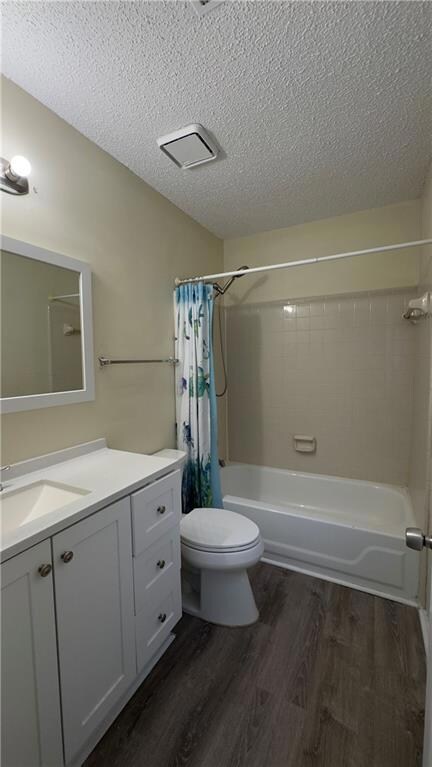 Full bath with shower / bathtub combination with curtain, vanity, dark wood-style flooring, and a textured ceiling