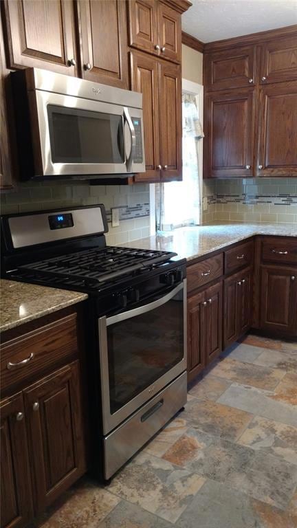 Kitchen featuring stainless steel appliances, backsplash, and light stone counters