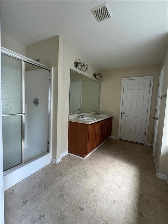 Full bath featuring double vanity, a shower stall, and light floors