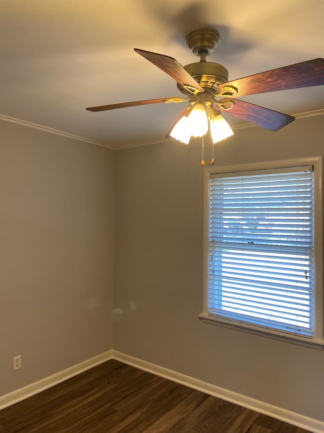 Empty room with dark wood-style flooring, a ceiling fan, baseboards, and crown molding