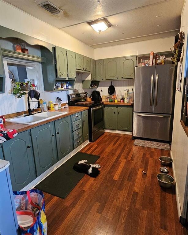 Kitchen with stainless steel fridge, electric stove, sink, green cabinets, and dark hardwood / wood-style flooring