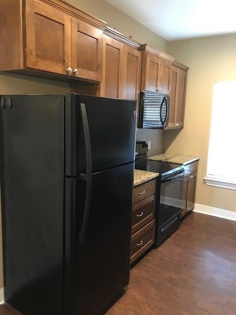 Kitchen with black appliances, dark wood-style floors, light stone countertops, and brown cabinetry
