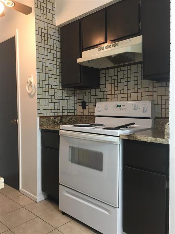 Kitchen with electric stove, ventilation hood, light tile patterned floors, and tasteful backsplash