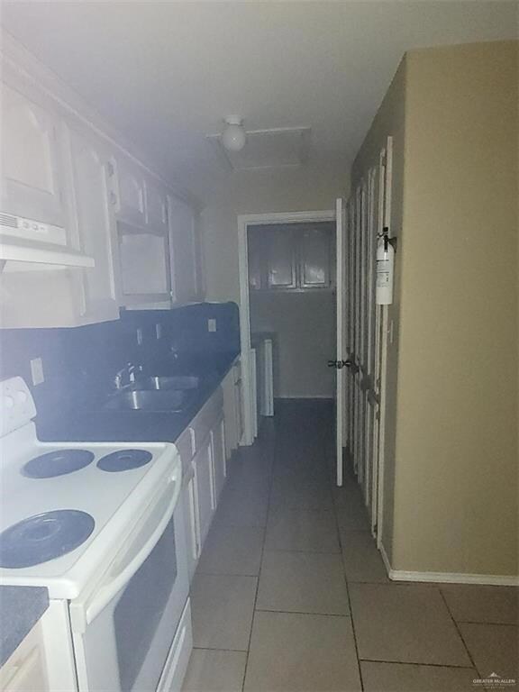 Kitchen with sink, white cabinets, tile patterned flooring, and white range with electric stovetop