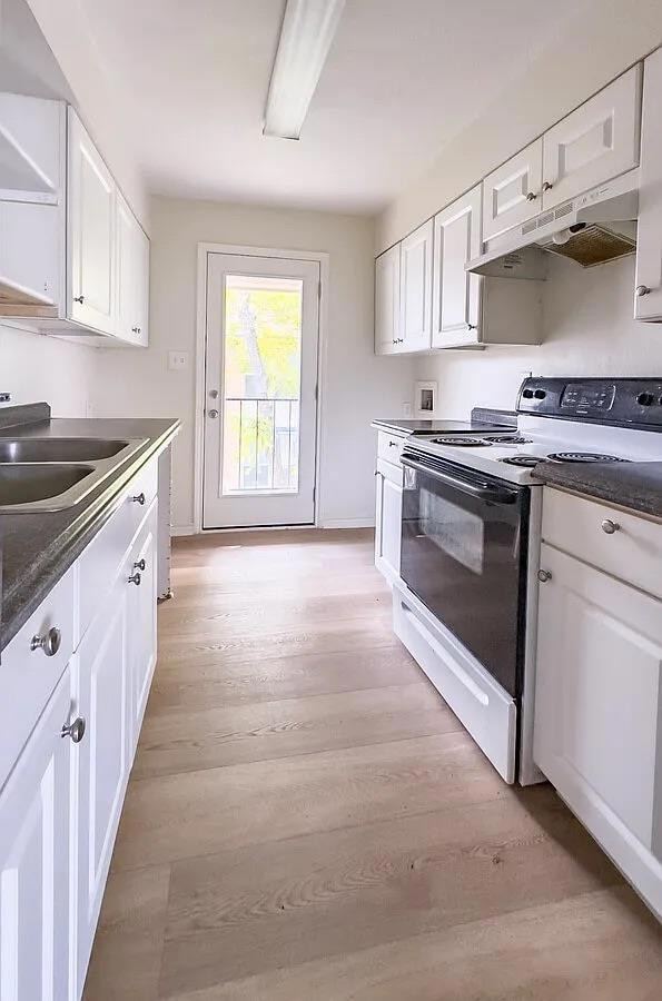 Kitchen with electric range, white cabinets, under cabinet range hood, and light wood-type flooring