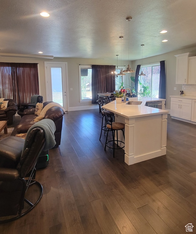 Kitchen featuring white cabinets, a kitchen breakfast bar, a textured ceiling, pendant lighting, and a large island
