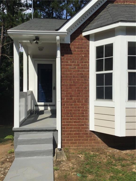 Doorway to property with brick siding and a shingled roof