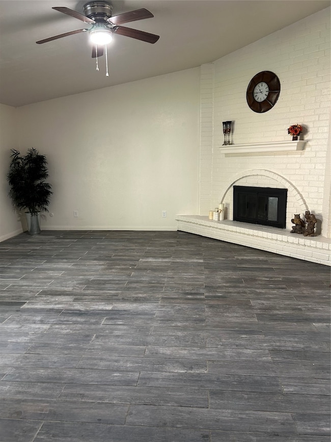 Living room with a brick fireplace, ceiling fan, and dark wood-style floors