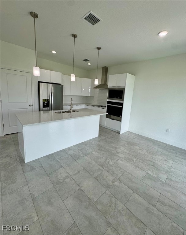 Kitchen with white cabinetry, decorative light fixtures, stainless steel appliances, an island with sink, and wall chimney range hood