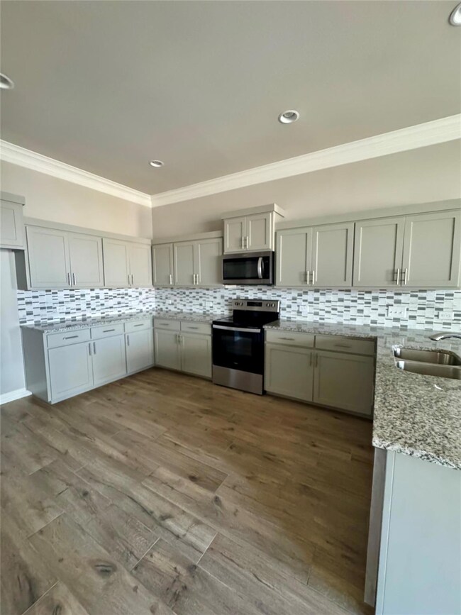 Kitchen featuring backsplash, ornamental molding, appliances with stainless steel finishes, light stone countertops, and wood finished floors