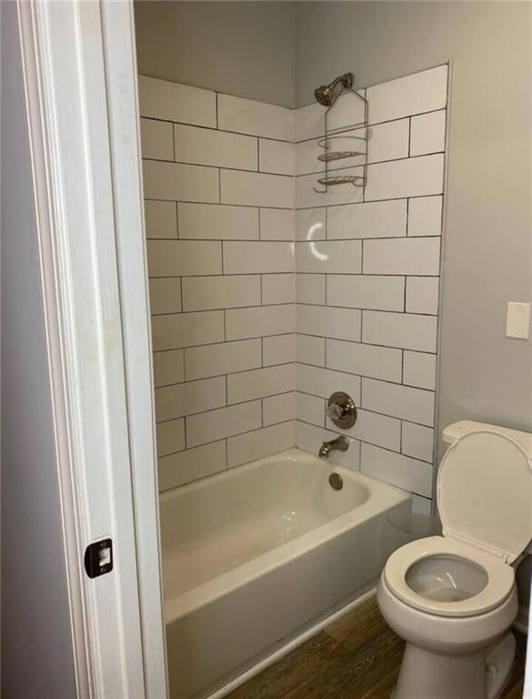 Full bathroom with washtub / shower combination, toilet, and wood finished floors