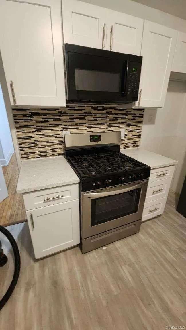 Kitchen with stainless steel gas range oven, black microwave, white cabinetry, and light wood-style flooring
