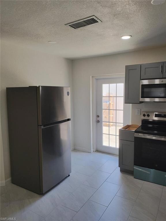 Kitchen with appliances with stainless steel finishes, gray cabinets, and a textured ceiling