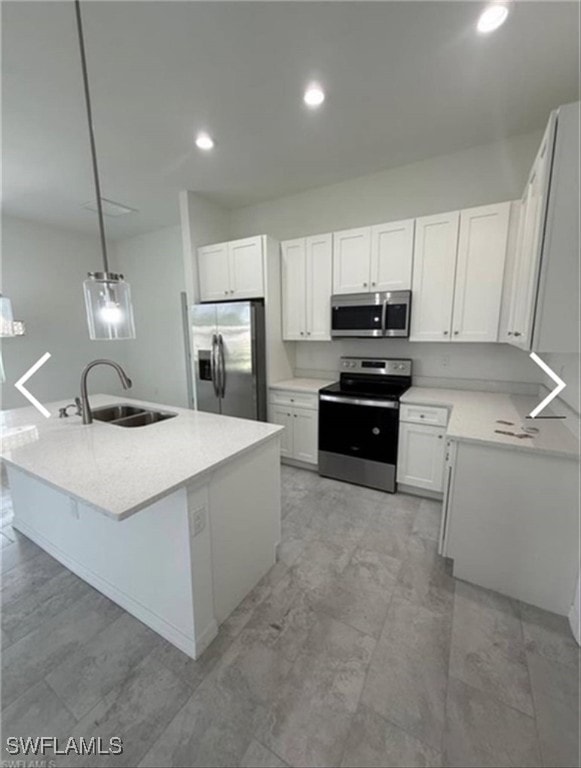 Kitchen featuring appliances with stainless steel finishes, a center island with sink, hanging light fixtures, white cabinetry, and recessed lighting