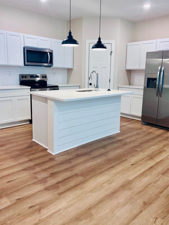 Kitchen with appliances with stainless steel finishes, light countertops, white cabinets, light wood finished floors, and recessed lighting