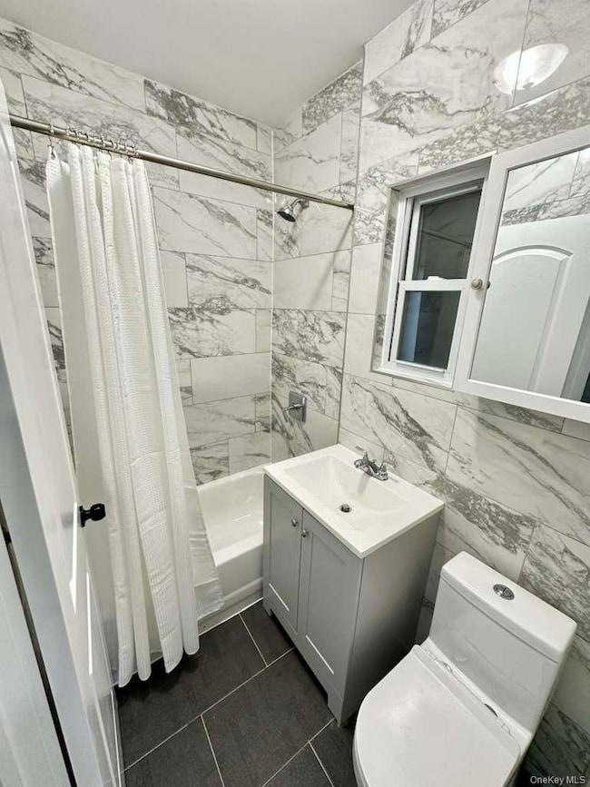 Bathroom with tile walls, vanity, shower / tub combo, and dark tile patterned flooring