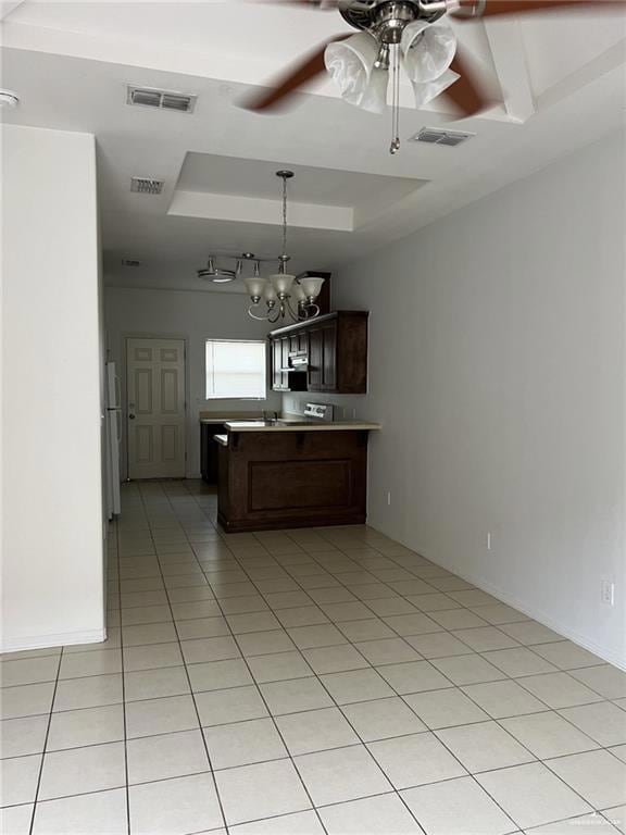 Kitchen with a tray ceiling, a ceiling fan, a peninsula, light tile patterned floors, and a chandelier