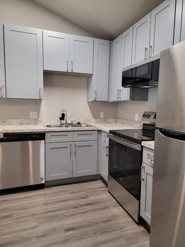 Kitchen featuring appliances with stainless steel finishes, gray cabinetry, light wood finished floors, and light stone countertops