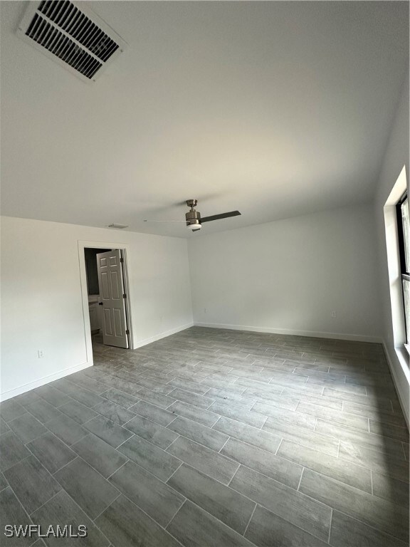 Unfurnished room with a ceiling fan, wood finish floors, visible vents, and baseboards