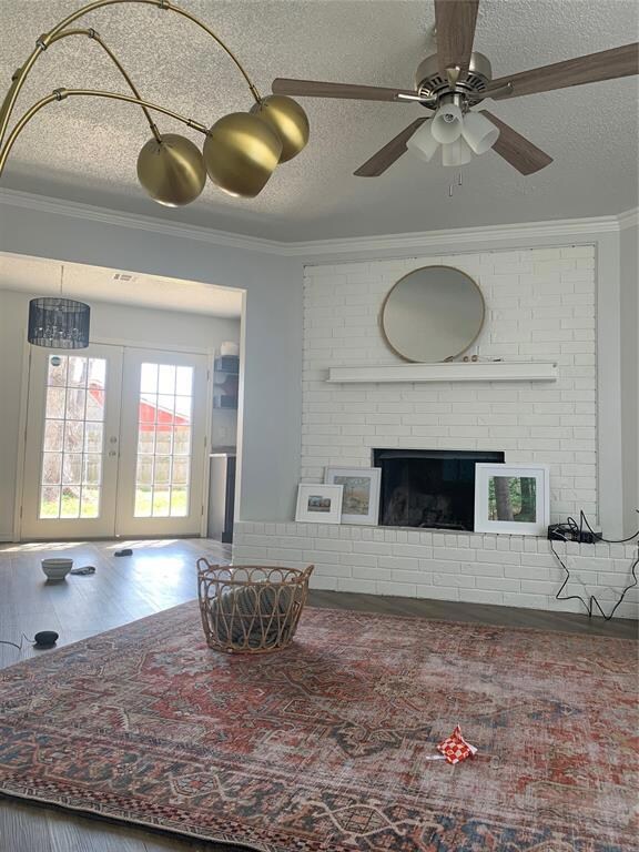 Living room with crown molding, a textured ceiling, french doors, ceiling fan, and a fireplace