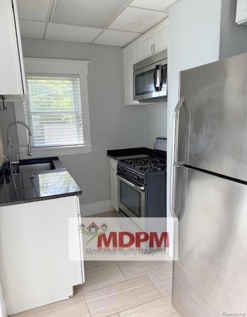 Kitchen featuring stainless steel appliances, white cabinets, light tile patterned floors, and a paneled ceiling