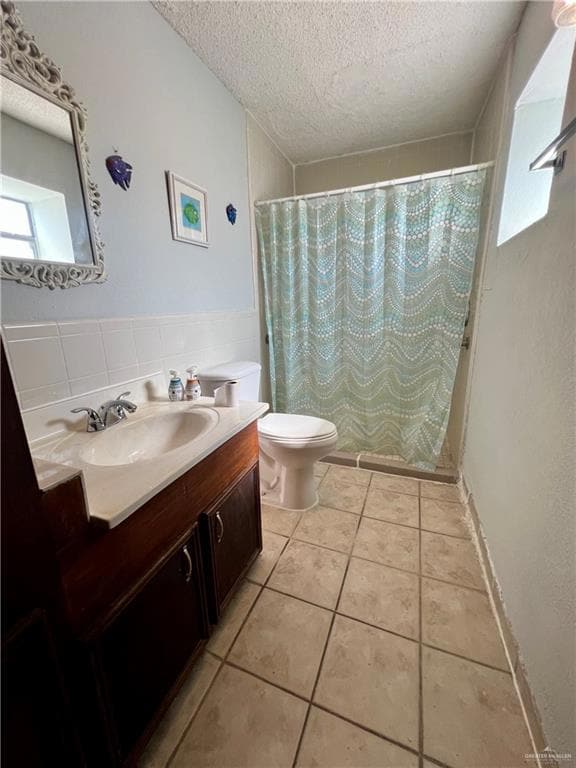 Bathroom featuring vanity, light tile patterned flooring, tile walls, and a textured ceiling