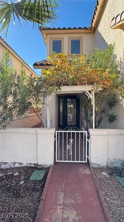 Property entrance featuring a gate, stucco siding, and a tile roof