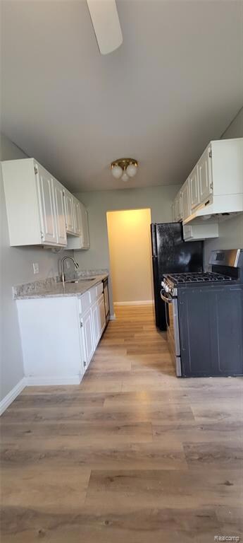 Kitchen featuring stainless steel gas range, light wood-type flooring, white cabinets, light stone countertops, and under cabinet range hood