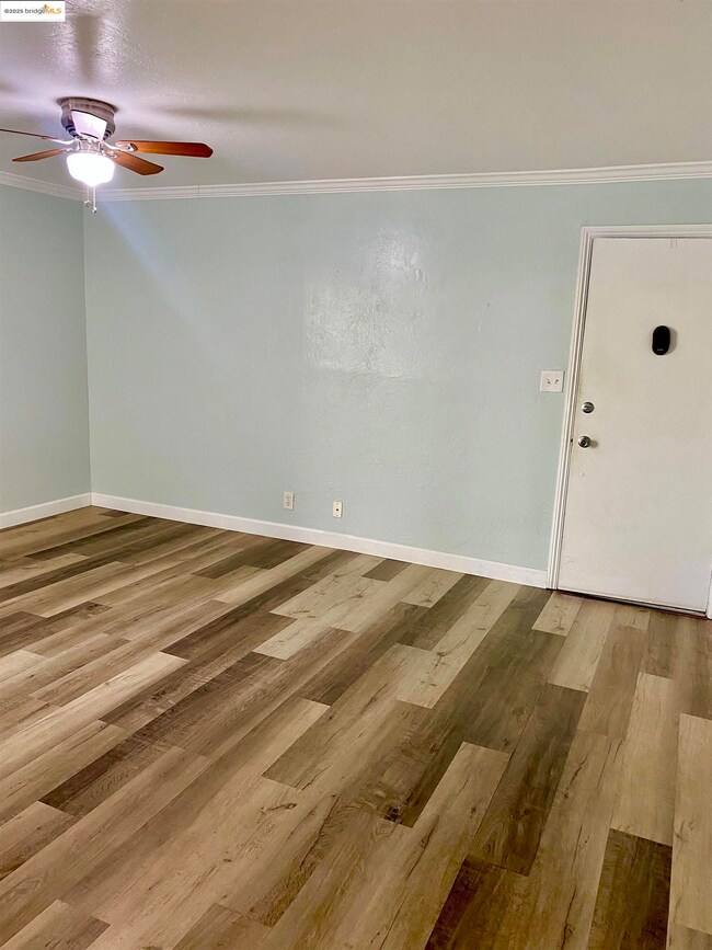 Empty room with wood laminate floors, ceiling fan, crown molding, and baseboards