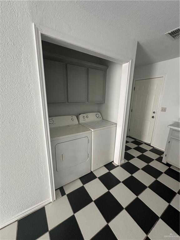 Laundry area featuring dark flooring, separate washer and dryer, cabinet space, a textured ceiling, and a textured wall
