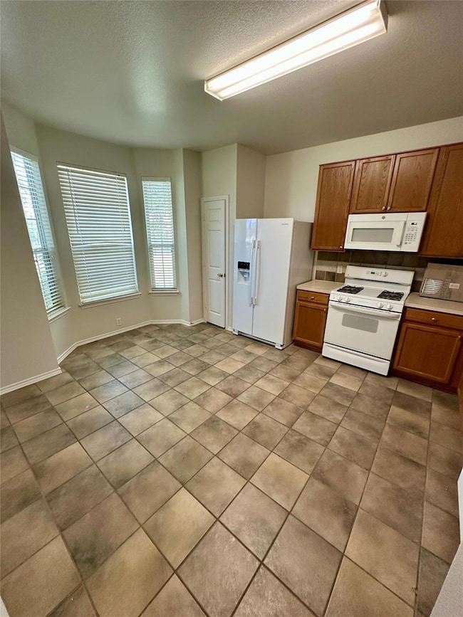 Kitchen with white appliances, brown cabinets, light tile patterned flooring, a textured ceiling, and light countertops