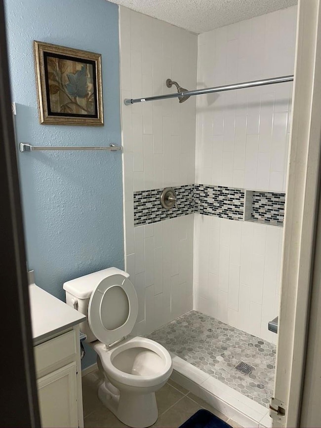 Full bath with vanity, a textured wall, a stall shower, tile patterned flooring, and a textured ceiling