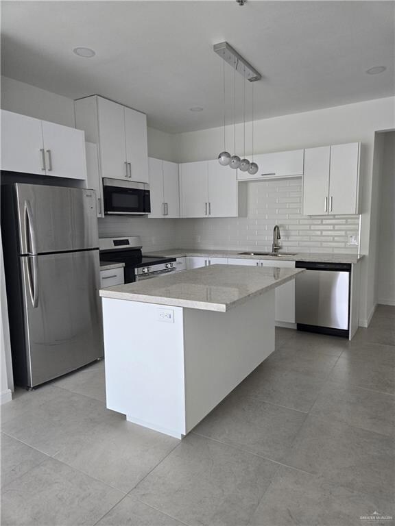 Kitchen with appliances with stainless steel finishes, a center island, decorative backsplash, white cabinetry, and hanging light fixtures