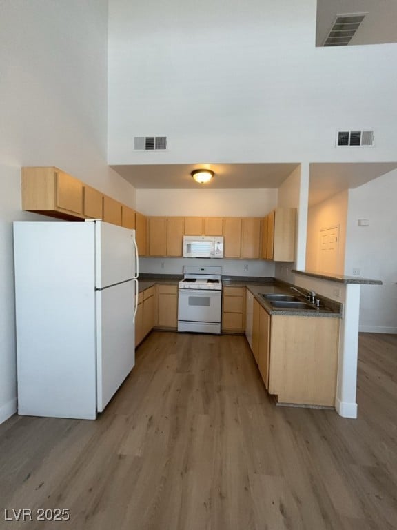 Kitchen featuring light brown cabinetry, white appliances, a high ceiling, light wood-type flooring, and dark countertops