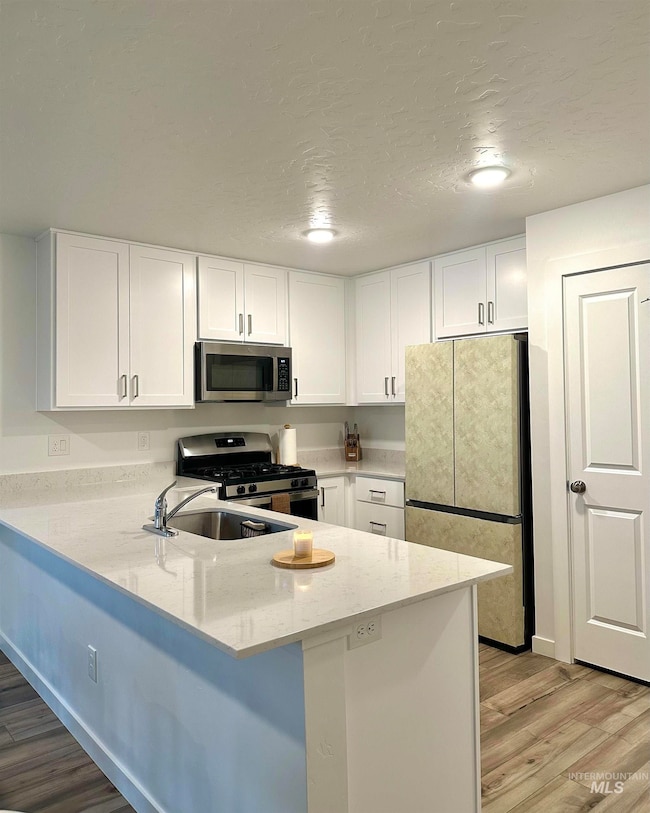 Kitchen with appliances with stainless steel finishes, white cabinetry, light wood-style floors, and a textured ceiling