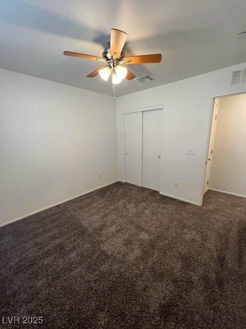 Unfurnished bedroom with dark carpet, a closet, and a ceiling fan