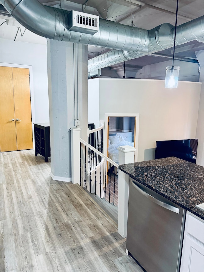 Kitchen featuring stainless steel dishwasher, dark stone counters, light wood-style flooring, pendant lighting, and white cabinetry