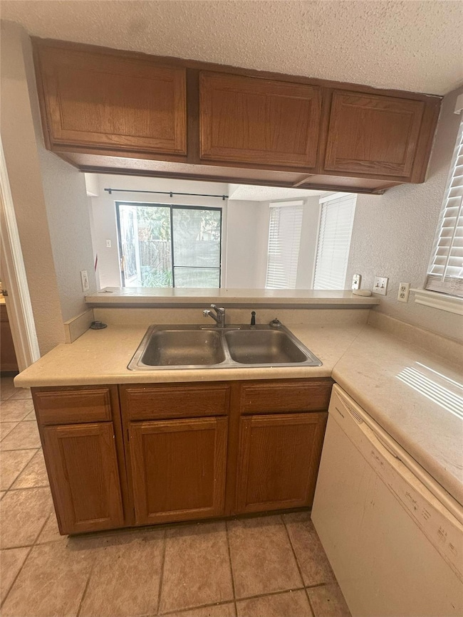 Kitchen with dishwasher, a textured ceiling, brown cabinetry, light countertops, and healthy amount of natural light
