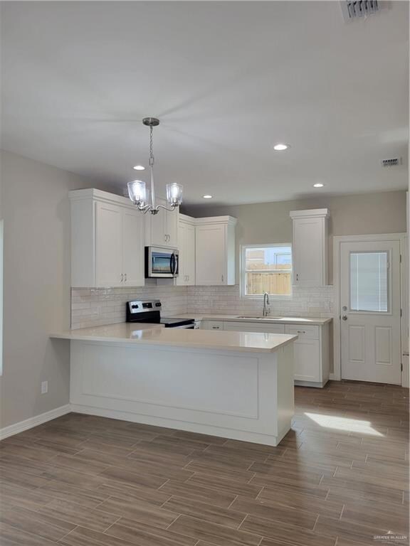 Kitchen with an inviting chandelier, decorative light fixtures, backsplash, white cabinets, and stove