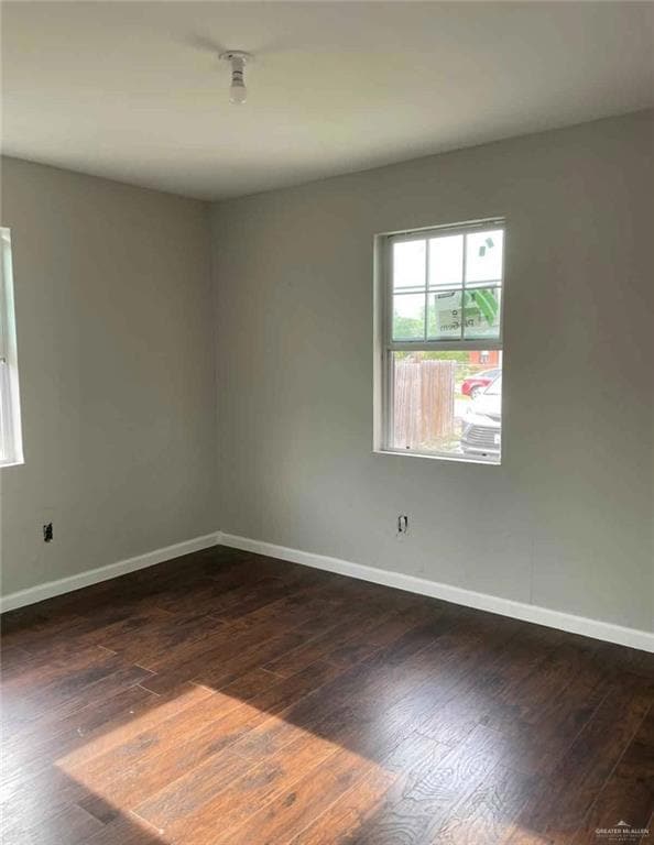 Spare room featuring baseboards and dark wood-style floors