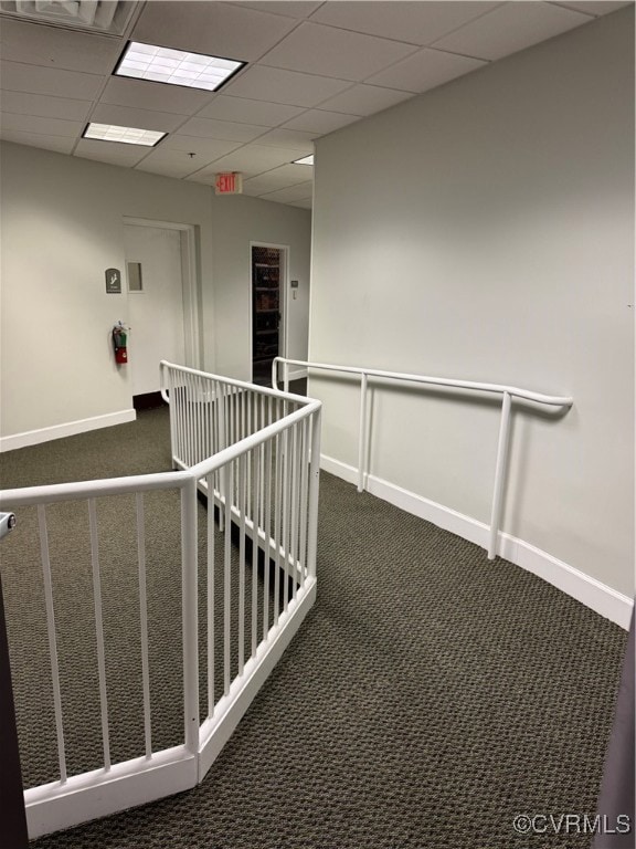 Hallway featuring baseboards, dark carpet, and a d