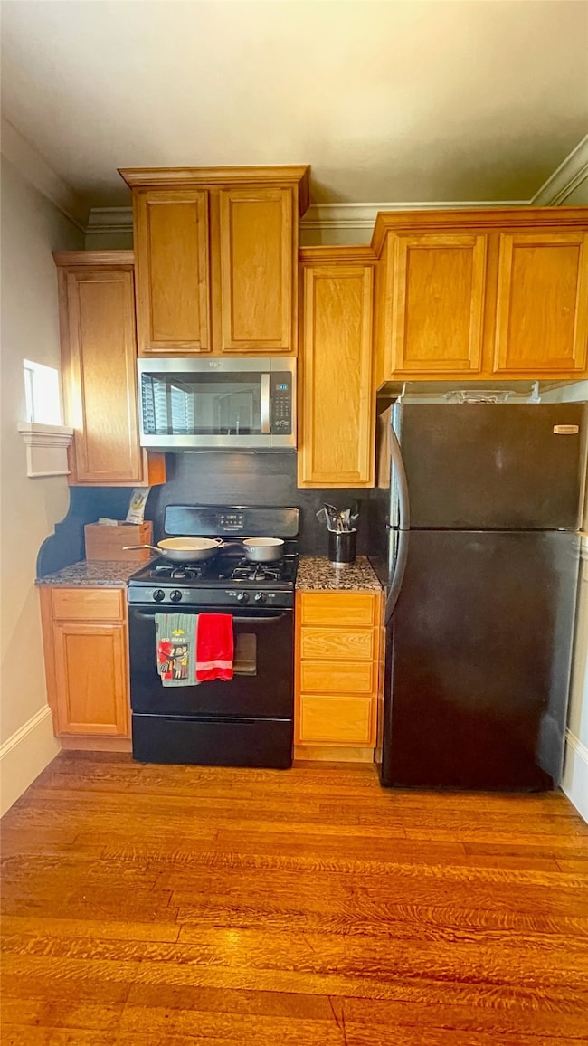 Light-filled kitchen featuring gas range, built-in microwave, refrigerator and hardwood floors.