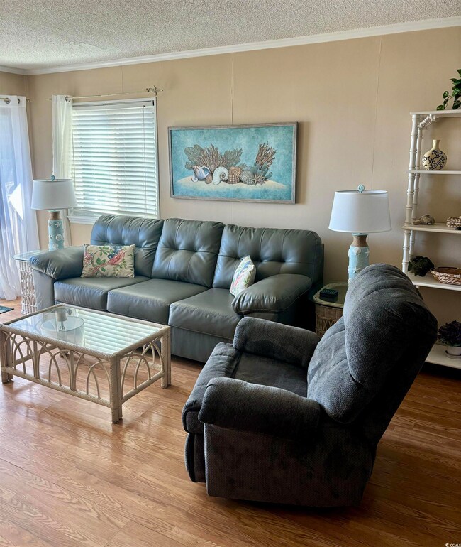 Living room with ornamental molding, light wood-type flooring, and a textured ceiling