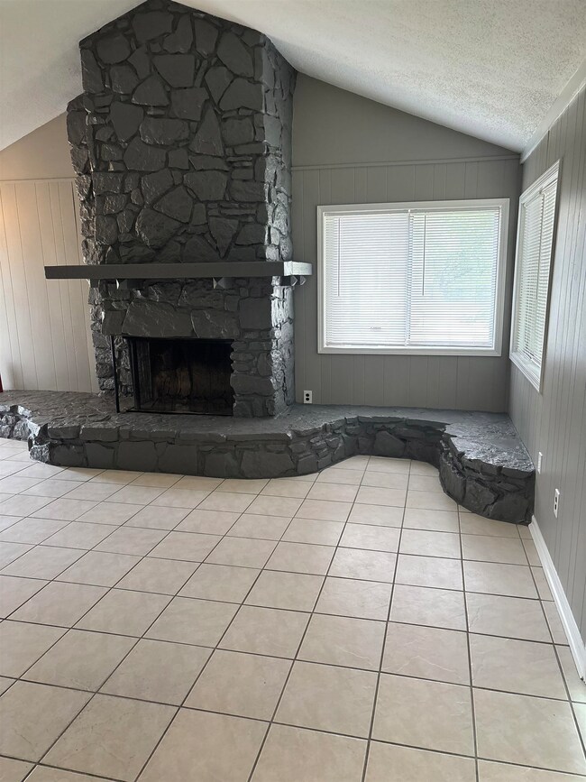 Unfurnished living room featuring vaulted ceiling, tile patterned flooring, and a stone fireplace