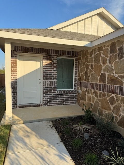 Doorway to property with brick siding and roof with shingles