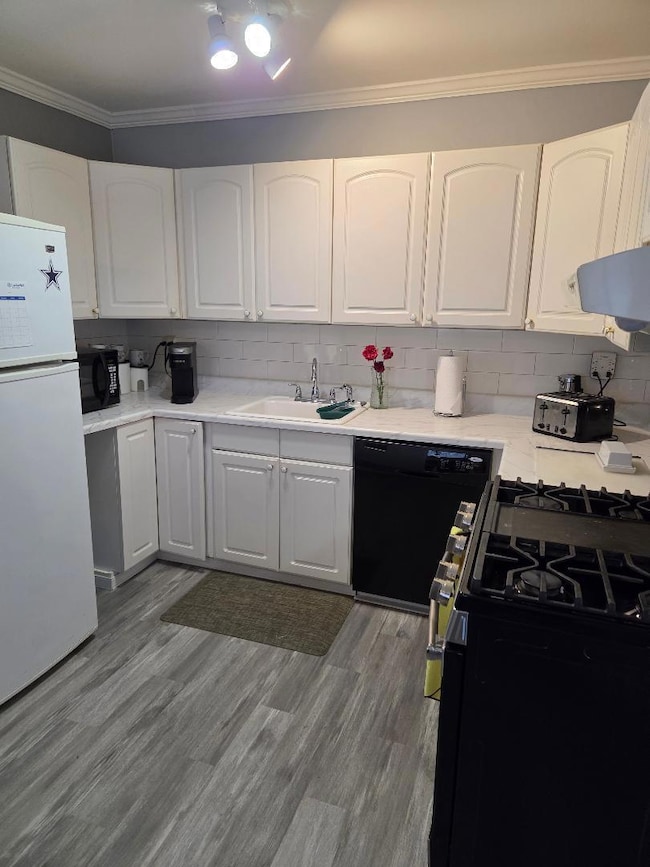 Kitchen featuring black appliances, ornamental molding, a sink, and white cabinets