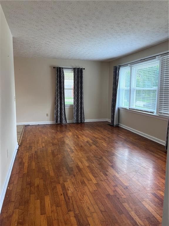 Empty room with dark wood-style flooring, a textured ceiling, and baseboards
