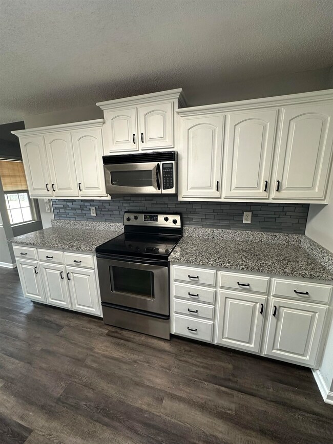 Kitchen featuring white cabinetry, appliances with stainless steel finishes, dark wood finished floors, light stone counters, and a textured ceiling