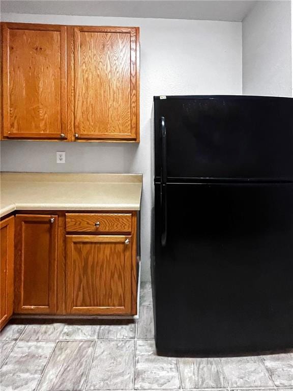 Kitchen with freestanding refrigerator, light countertops, and brown cabinets
